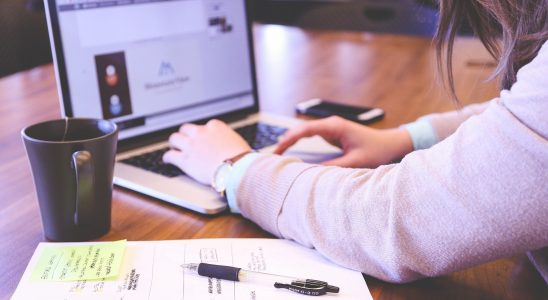 Personne travaillant sur son ordinateur, une table et un bloc se trouvent à sa gauche.