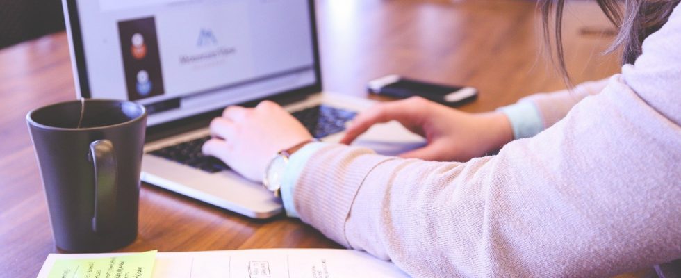 Personne travaillant sur son ordinateur, une table et un bloc se trouvent à sa gauche.